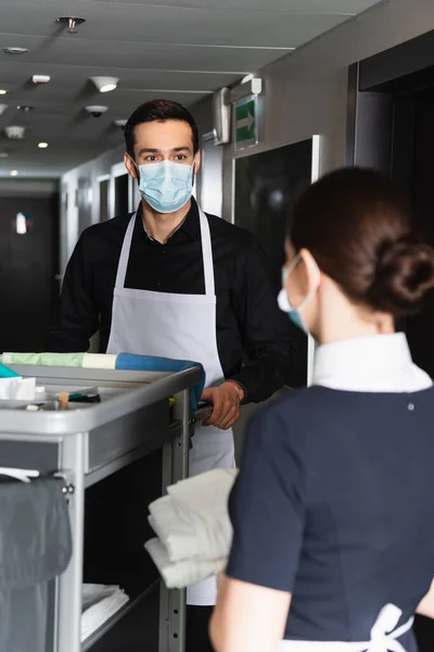 Haushälterin Medizinischer Maske Sieht Verschwommenes Dienstmädchen Der Nähe Des Hauswirtschaftswagens — Stockfoto