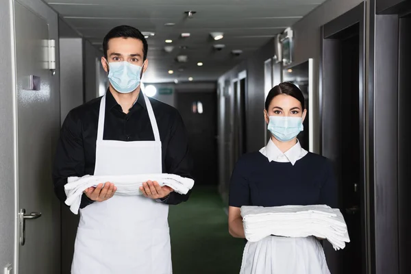 Empregadas Domésticas Uniforme Máscaras Médicas Segurando Lençóis Limpos Corredor Hotel — Fotografia de Stock