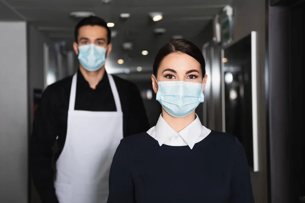 Uklízečky Uniformách Lékařských Maskách Při Pohledu Kamery Chodbě Hotelu — Stock fotografie