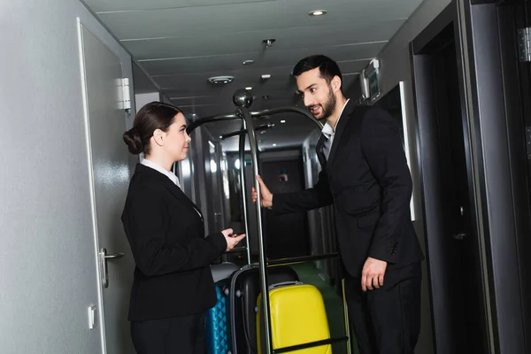 Réceptionniste Souriant Pointant Avec Main Près Groom Près Chariot Bagages — Photo