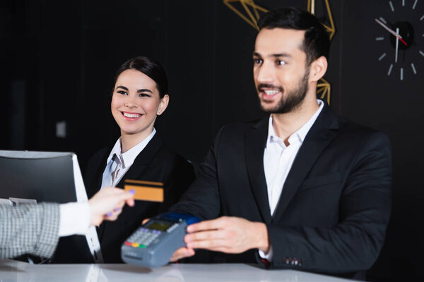 happy receptionists looking at tourist paying with credit card 