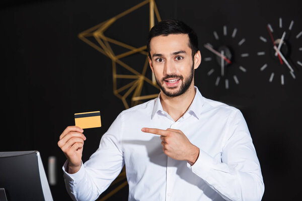 bearded receptionist pointing at credit card and smiling in hotel 