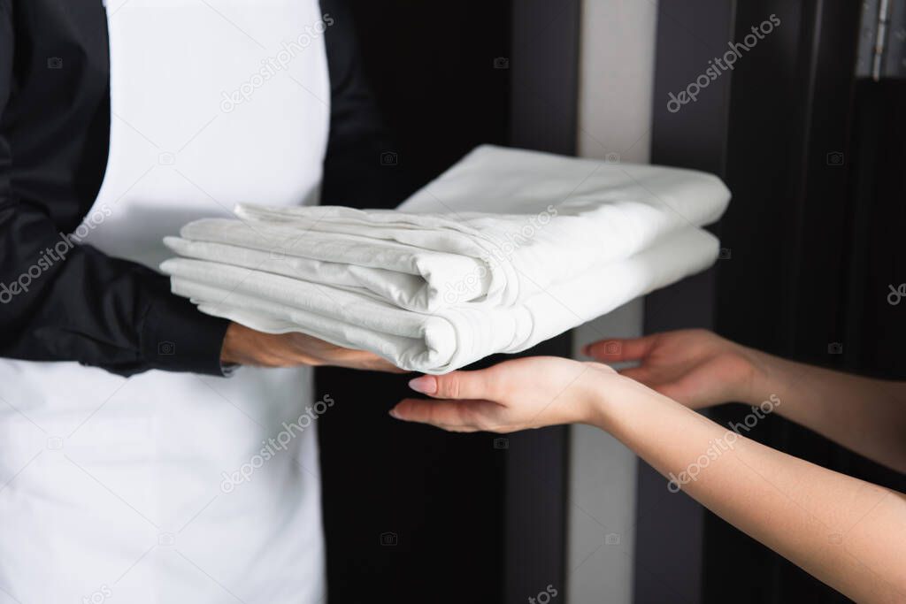 cropped view of maid housekeeper giving clean bed sheets to maid