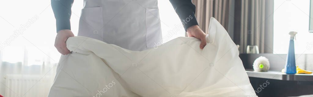 cropped view of housekeeper changing bedding in hotel room, banner