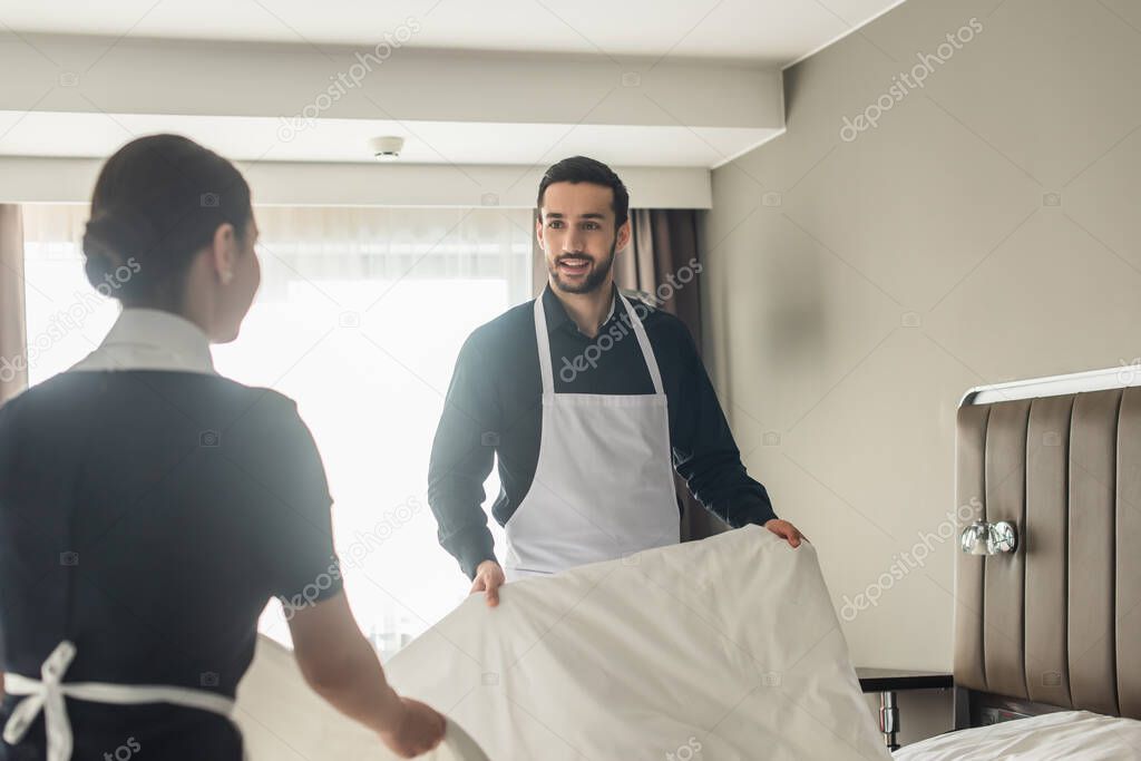 happy housekeepers changing bedding in hotel room 