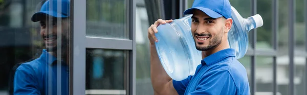 Glimlachende Arabische Koerier Met Fles Water Buurt Van Gebouw Spandoek — Stockfoto