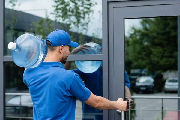 Muselman Deliveryman Hållande Flaska Vatten Stund Öppna Dörr Byggnad — Stockfoto