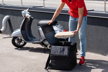 Kırmızı üniformalı kuryenin termometre çantasının yanında pizza kutusu tutarken görüntüsü bulanık. 