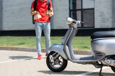 Scooter 'ın görüntüsü bulanık kuryenin yanında kahve eşliğinde açık havada kağıt torba. 