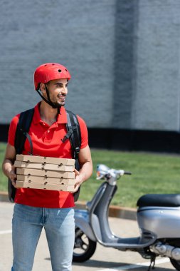 Neşeli Arap kurye dışarıda bulanık scooter 'ın yanında pizza kutuları tutuyor. 