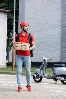 Kasklı Müslüman kurye dışarıda mobiletin yanında pizza kutuları tutuyor. 