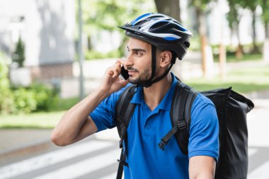 Kasklı genç müslüman teslimatçı dışarıda akıllı telefondan konuşuyor. 