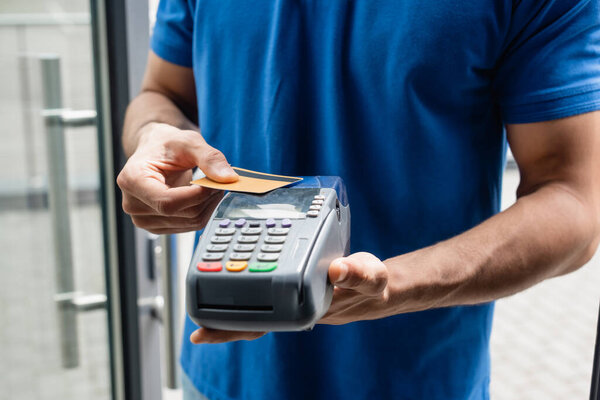 Cropped view of courier holding credit card and payment terminal outdoors 