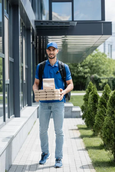 Pozytywny Muzułmański Kurier Trzymający Papierową Torbę Pudełka Pizzy Pobliżu Budynku — Zdjęcie stockowe