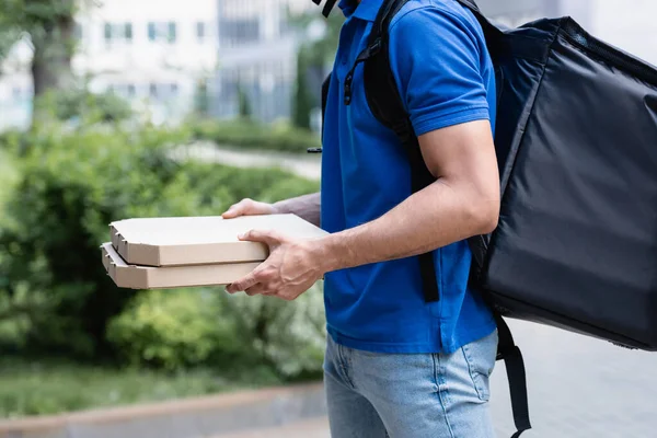 Termo sırt çantalı kuryenin açık havada karton pizza kutuları tutarken görüntüsü kesilmiş. 