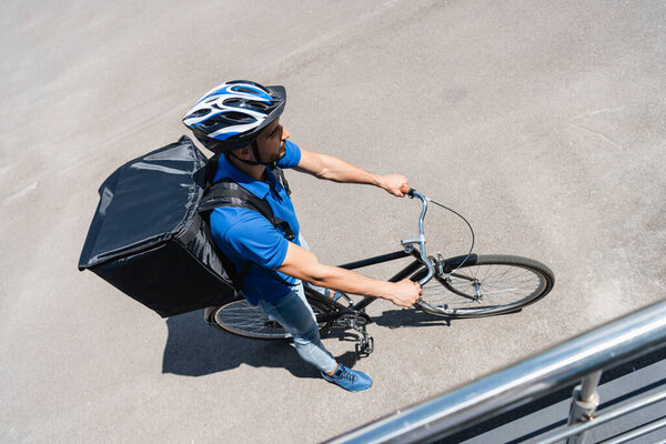 Overhead view of muslim courier with backpack riding bicycle outdoors 