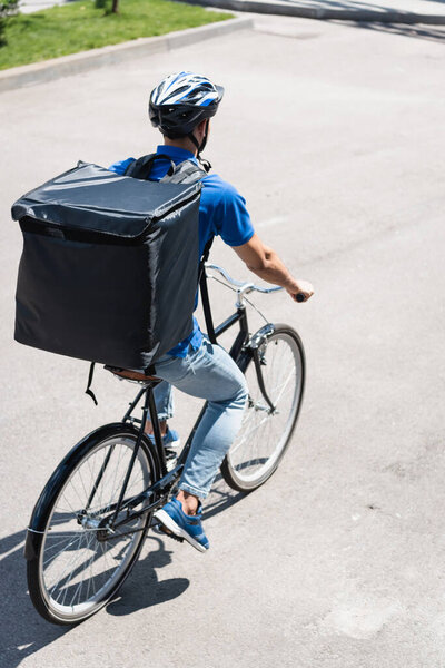 Young deliveryman with thermo backpack riding bicycle outdoors 