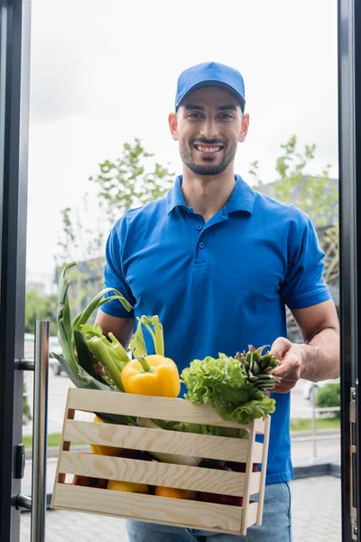 Sorrindo Árabe Entregador Segurando Caixa Com Legumes Perto Porta — Fotografia de Stock