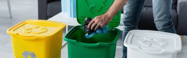 Evinde geri dönüşüm tabelası olan plastik poşetleri çöp kutusuna koyan adamın kırpılmış görüntüsü. 