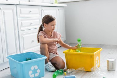 Girl sorting bottles in boxes with recycle sign in kitchen  clipart