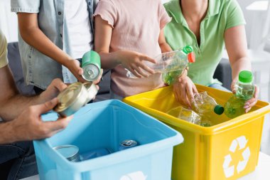 Aile ve çocukların çöp kutularını geri dönüşüm levhasıyla sıralamasının kırpılmış görüntüsü 