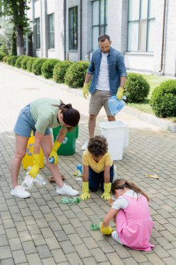 Lastik eldivenli aile, şehir sokaklarında çöp kutularının yakınındaki çöpleri ayırıyor. 