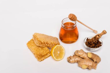 Bal kavanozu ahşap kaplamanın yanında, anason tohumlu kase, bal peteği, taze limon ve beyaz üzerine zencefil kökü.