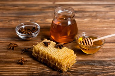 jar and bowls with honey and anise seeds near honeycomb on wooden table clipart
