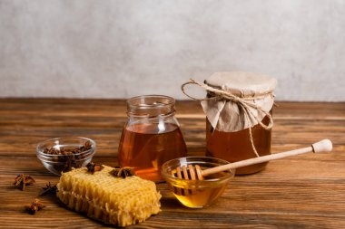 Balpeteğinin yanında ballı kavanozlar, ahşap masa üzerinde anason tohumları ve dipper ve gri arka plan