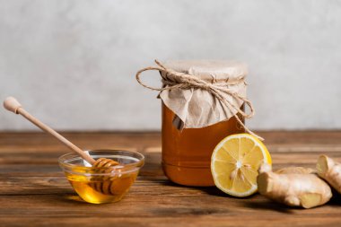 Sarı ballı kavanoz sulu limon, zencefil kökleri ve gri arka planda ahşap kaplama.