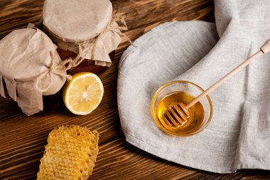 Taze limon, bal peteği ve ahşap masa üzerindeki el işi kağıtlarla kaplı kavanoz ve ballı çanak manzarası.