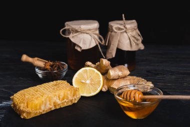 Bal peteği, taze limon, zencefil kökü ve anason tohumu ve bal dolu kaseler siyah üzerine izole edilmiş bulanık kavanozların yanında.