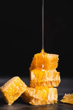 trickle of liquid honey dripping on cut honeycomb isolated on black clipart