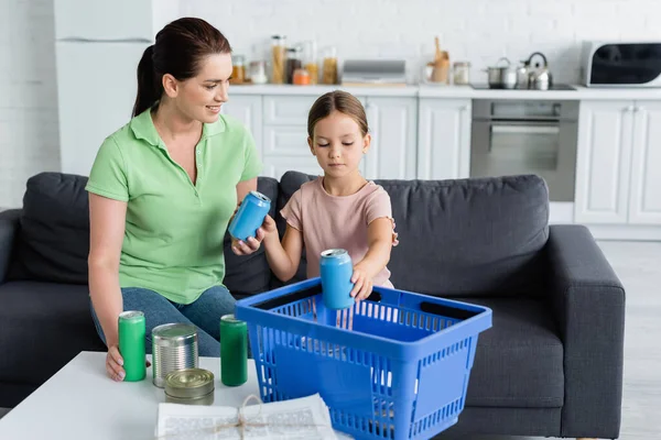 Smiling woman holding can while sorting trash with daughter in kitchen