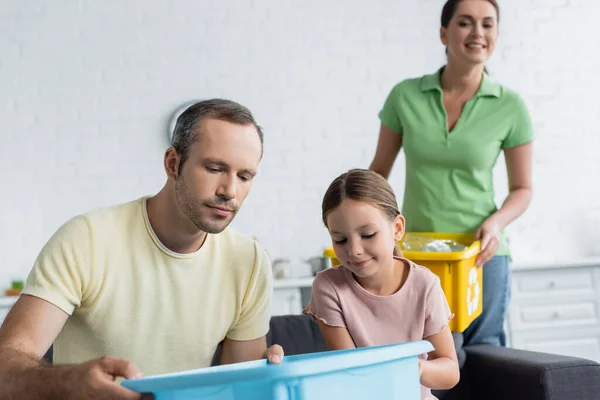 Stock image Man holding box near daughter and blurred wife with trash at home 