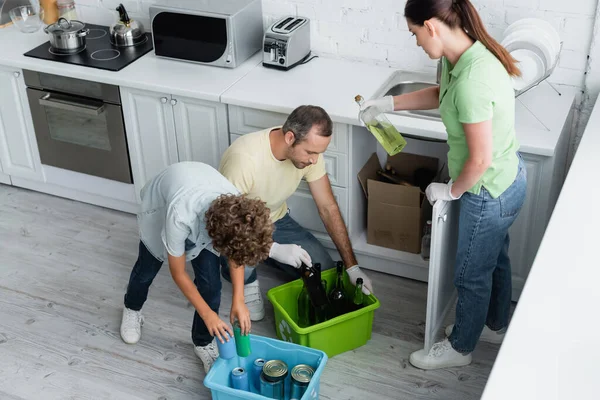 Family with son sorting trash in boxes in kitchen