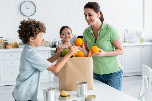 Positive Mother Children Taking Food Paper Bag Kitchen — Stock Photo, Image