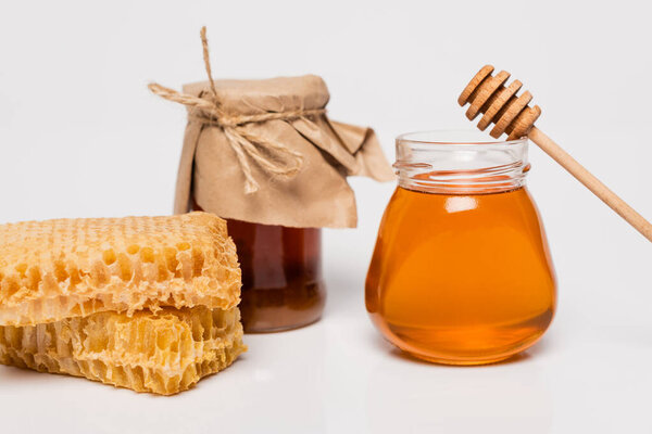 jars with yellow and brown honey near honeycomb and wooden dipper on white