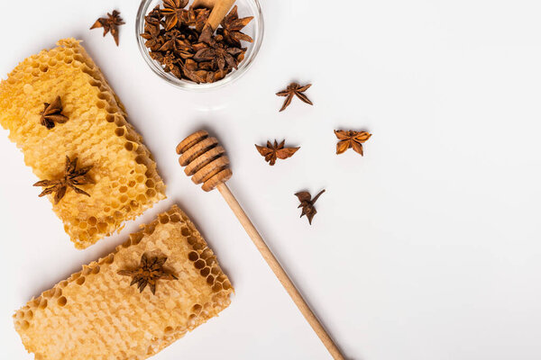 top view of honey dipper near honeycomb and bowl with anise seeds on white