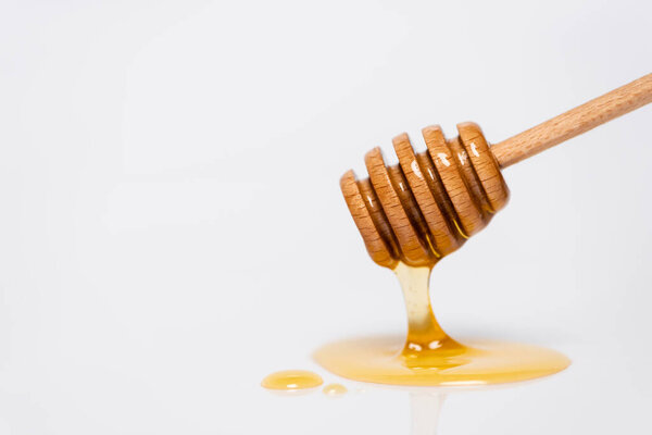 fresh, golden honey flowing from wooden dipper on white background