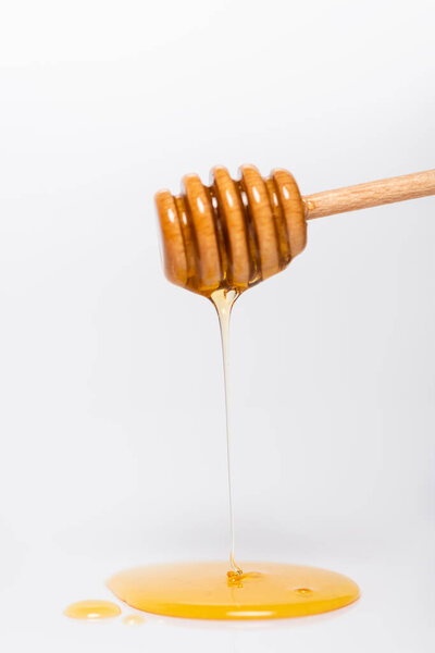 fresh, liquid honey flowing from wooden dipper on white background