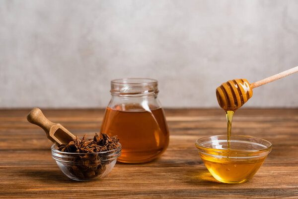 wooden dipper and scoop near jar and bowls with honey and anise seeds on grey marble background