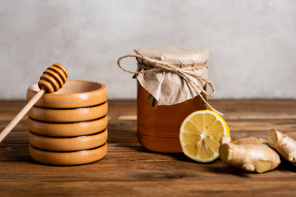 wooden container and dipper near half of fresh lemon, ginger root and jar with honey on grey background