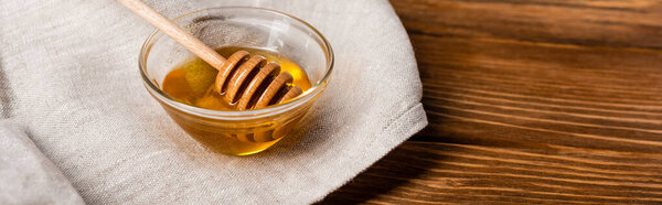 bowl with honey and dipper on linen napkin and wooden table, banner
