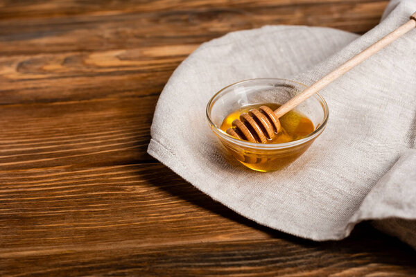 bowl with fresh honey and dipper on linen napkin and wooden surface