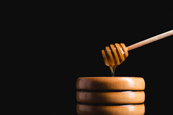 liquid honey flowing from dipper into small wooden barrel isolated on black