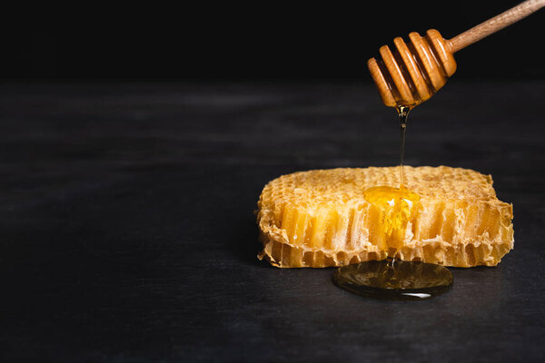 honeycomb near wooden dipper with flowing honey isolated on black