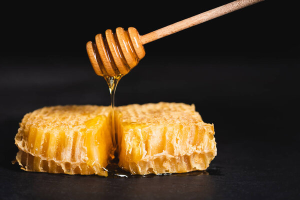 wooden dipper with liquid honey flowing on honeycomb isolated on black