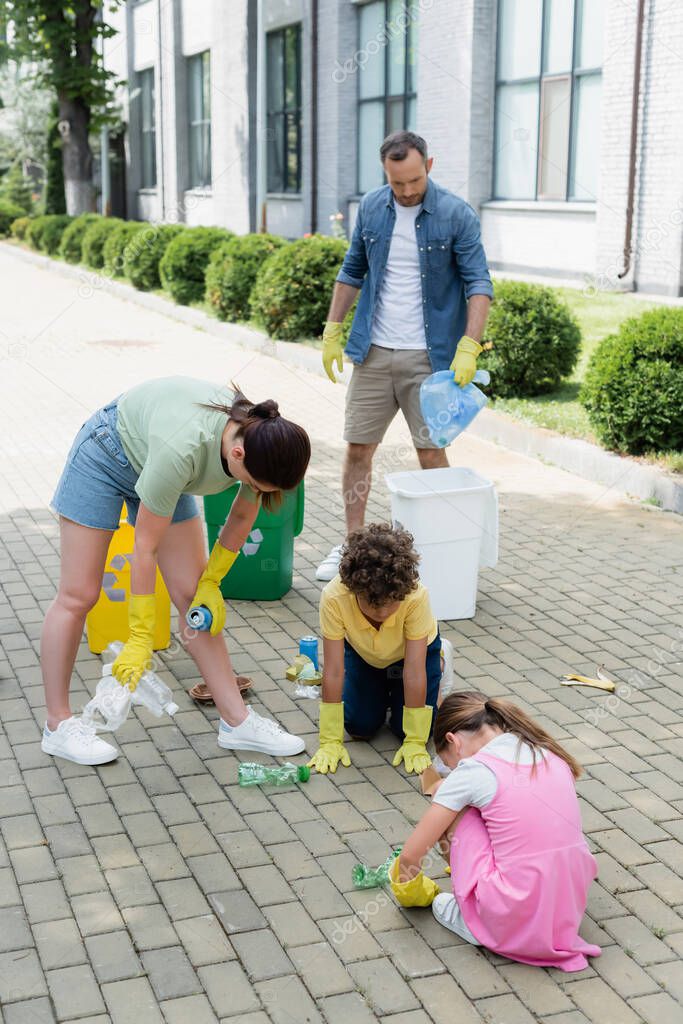 Family in rubber gloves sorting garbage near cans on urban street 