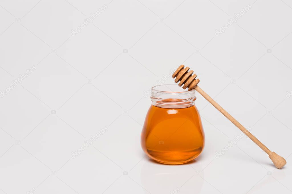 jar with fresh honey near wooden dipper on white background with copy space